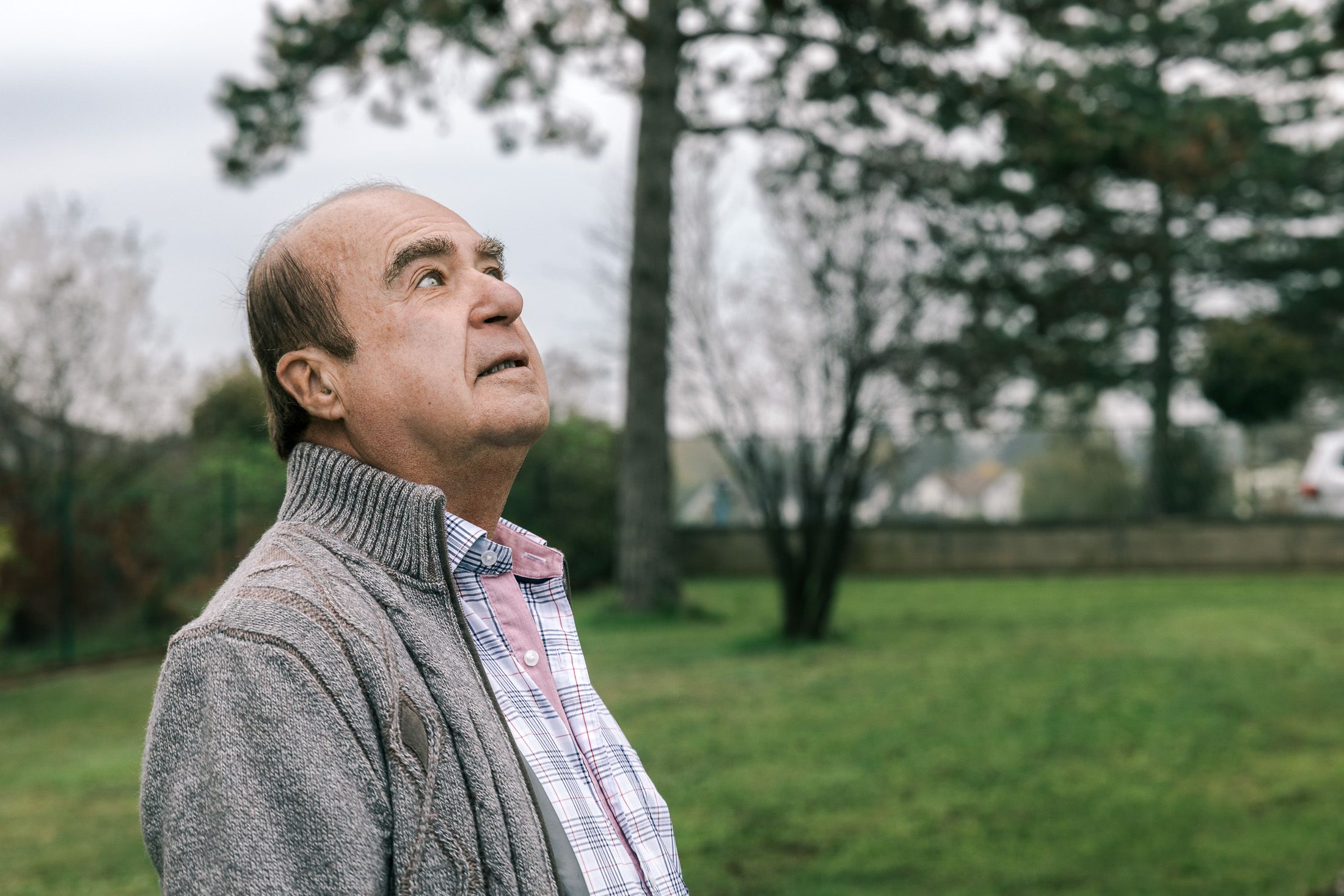 Johannes Besau in grauem Pullover, steht in seinem Garten und sieht in den Himmel.