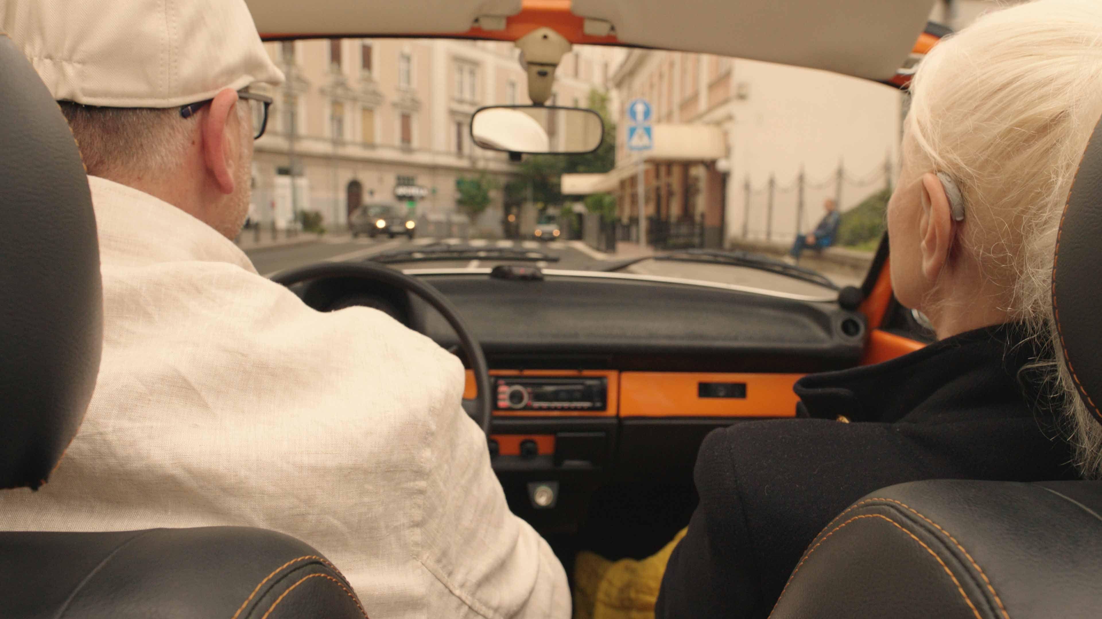Zena sijede kose sa slusnim aparatom sjedi u automobilu snimljena otpozadi