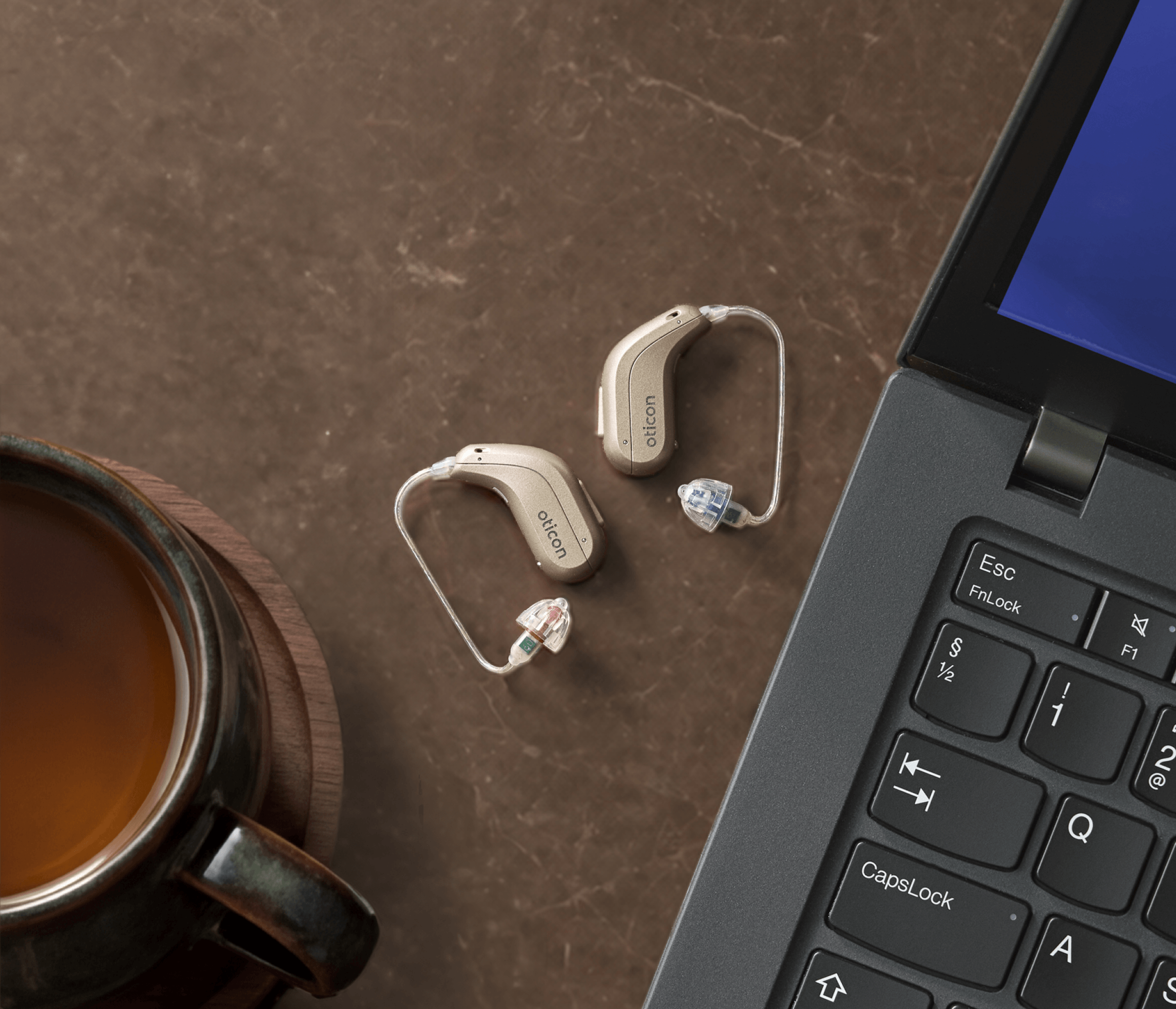 Neues Oticon Reveal auf Tisch neben Laptop und Kaffee