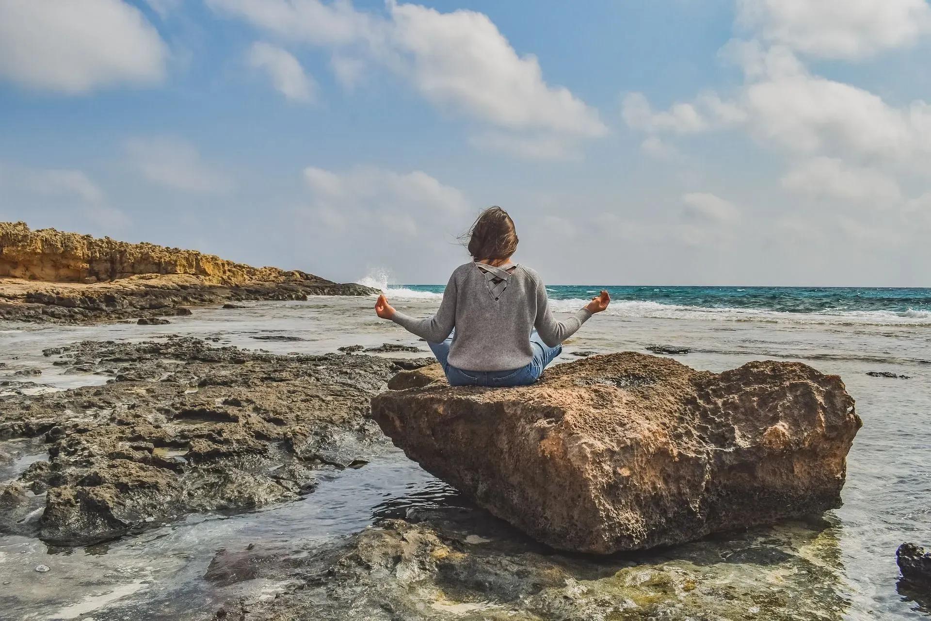 Žena meditira na kamenitoj obali mora, snimljena s leđa