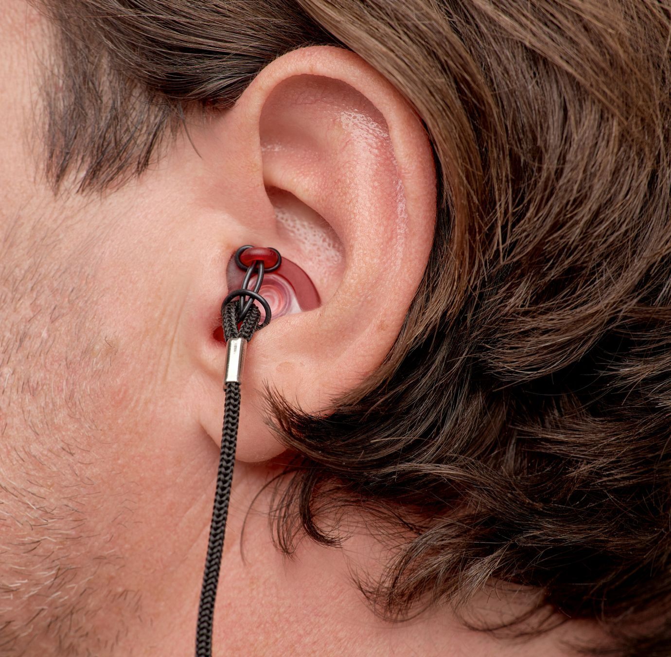 Detaljni prikaz silikonske Earwear zaštitnih čepića za uši sa crnim kanapom u uhu muškarca