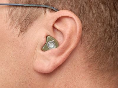 Detaljni prikaz Earwear zaštite za uši zelene boje u uhu muškarca sa naočarima