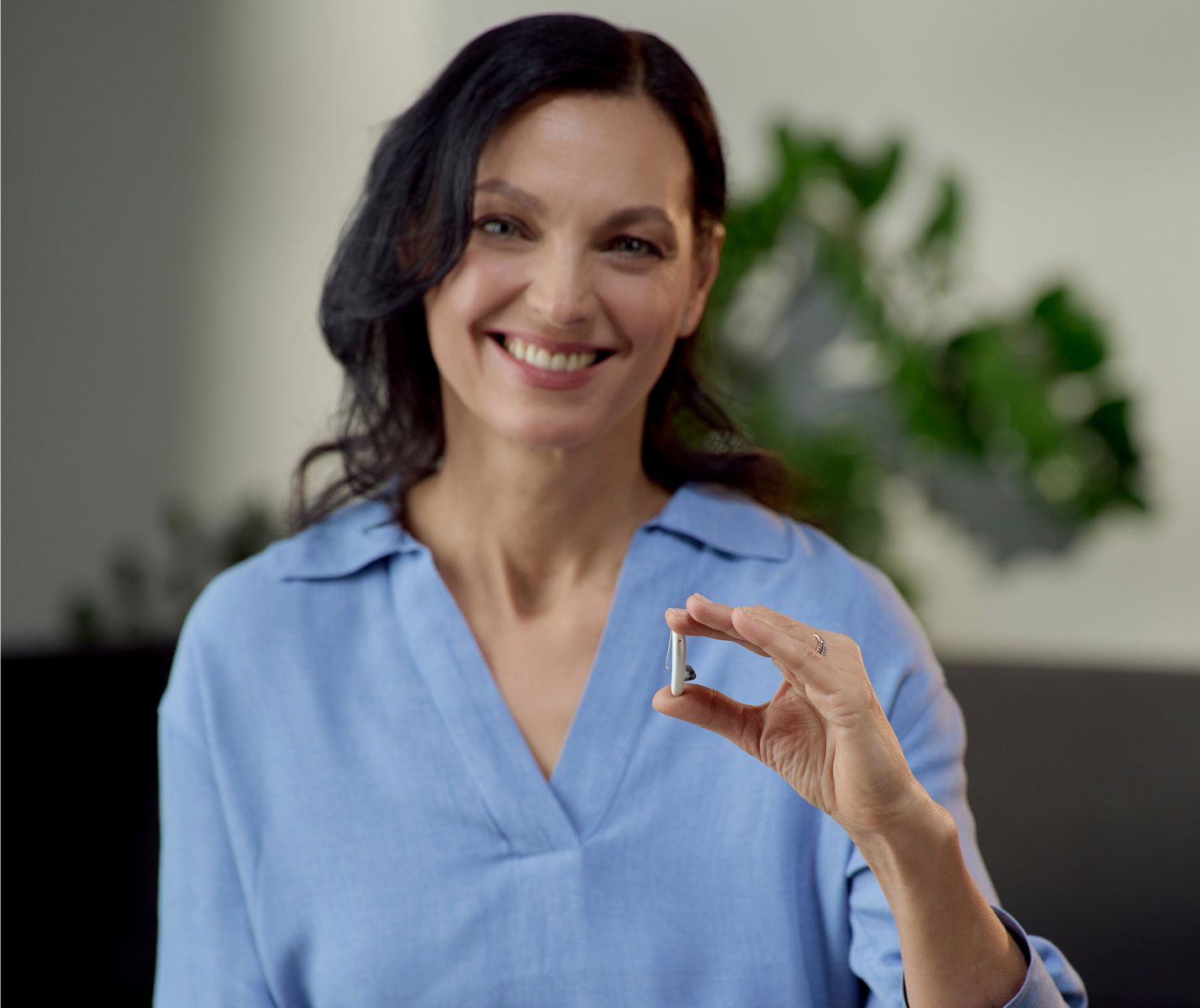 Frau mit schwarzen Haaren und Hörgerät in der Hand