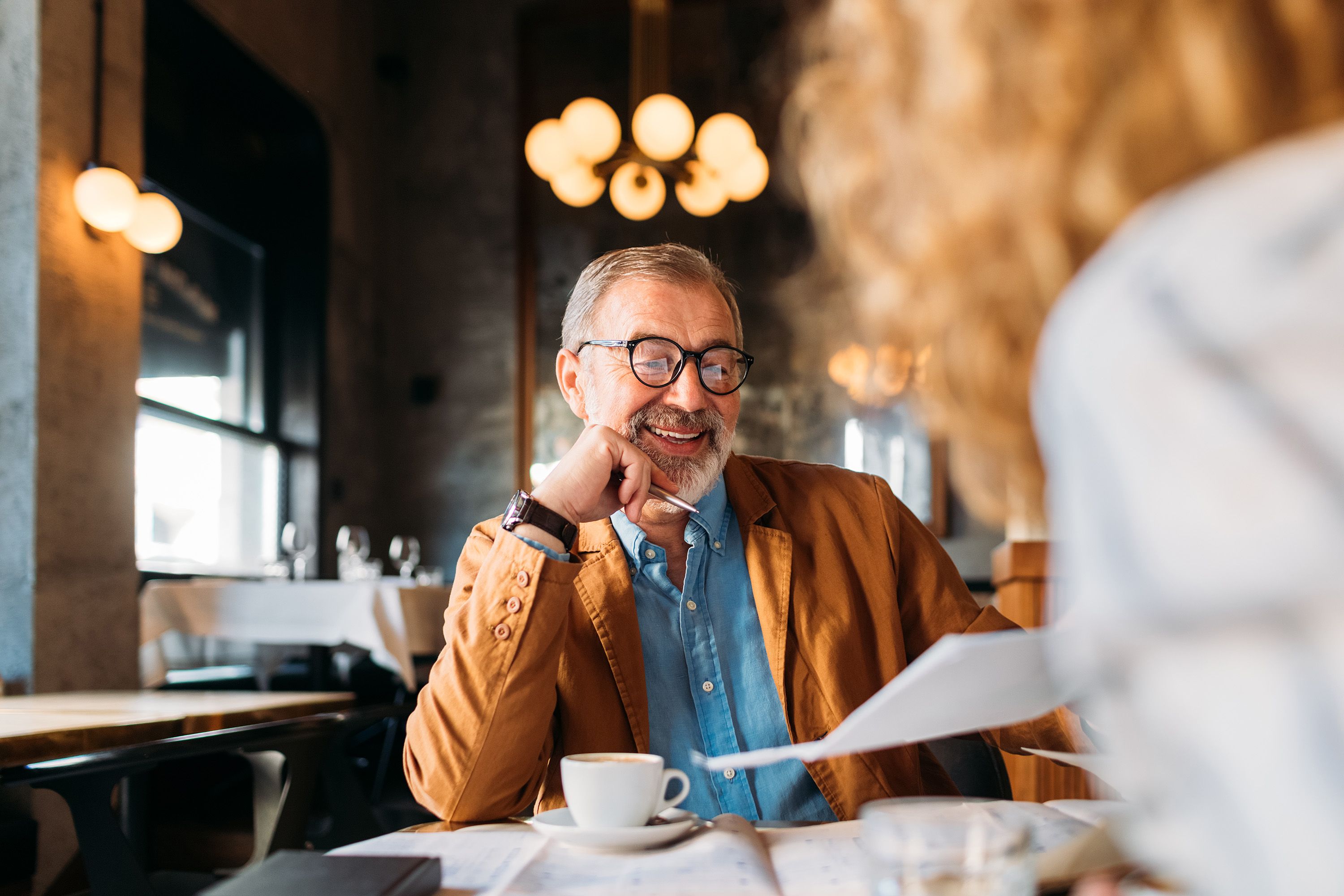 homme-age-avec-des-lunettes-souriant-dans-un-cafe-lors-dune-conversation-avec-une-femme