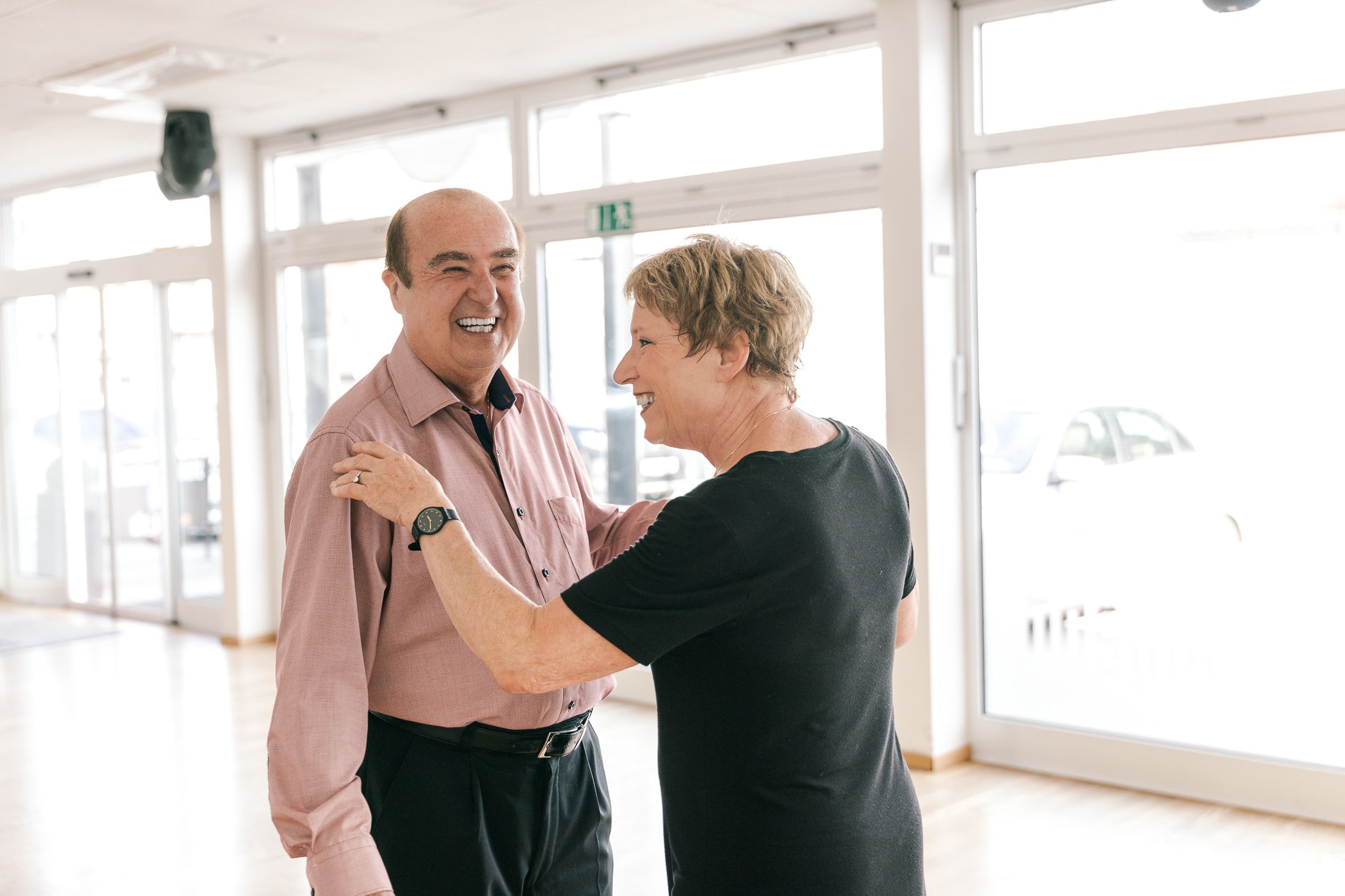 Johannes Besau in rosa Hemd beim Tanztraining mit seiner Tanzpartnerin. Sie setzten sich in Position und lächeln.