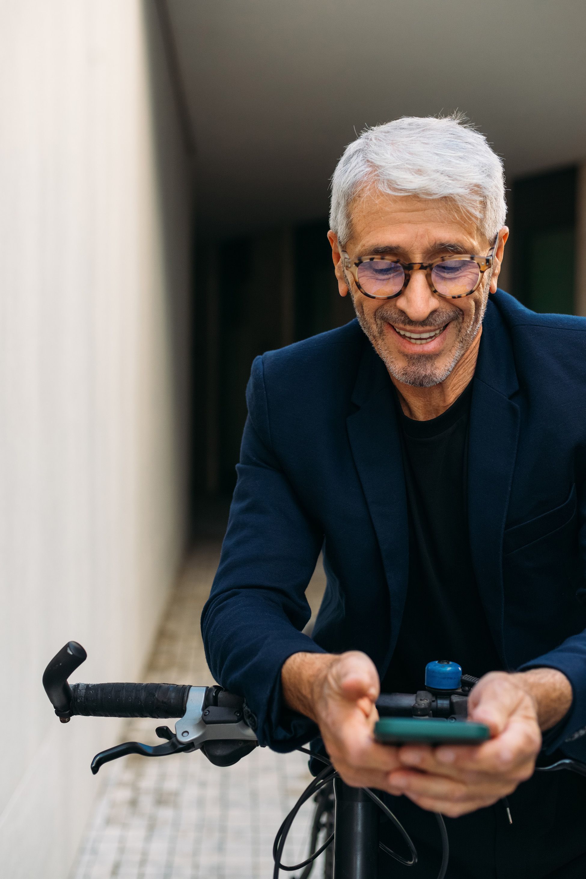Lachender Mann mit grauen Haaren und Brille steht mit Fahrrad und schaut auf Smartphone