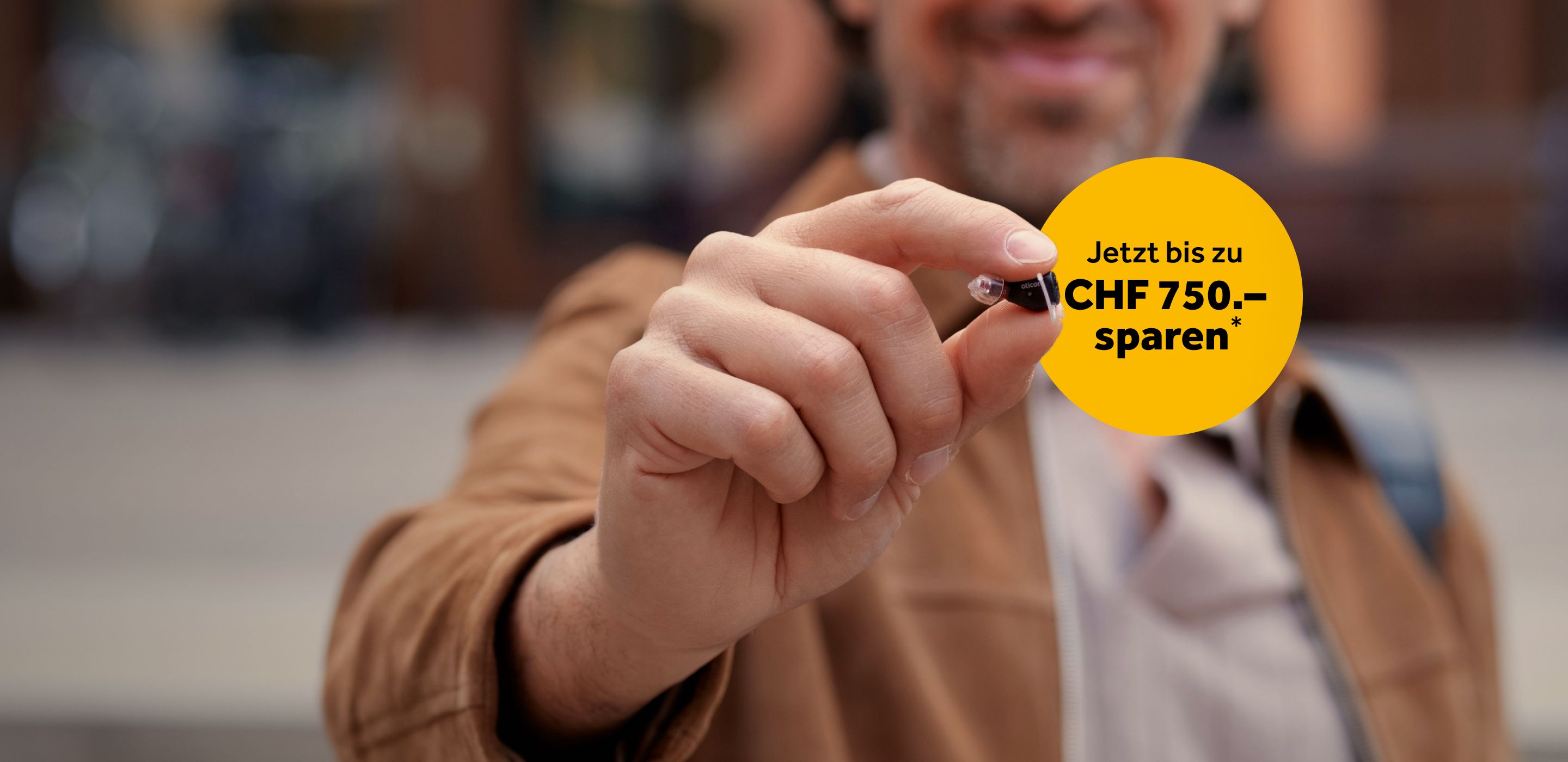 Mann mit Oticon Zeal in der Hand und Text bis zu 750 CHF sparen