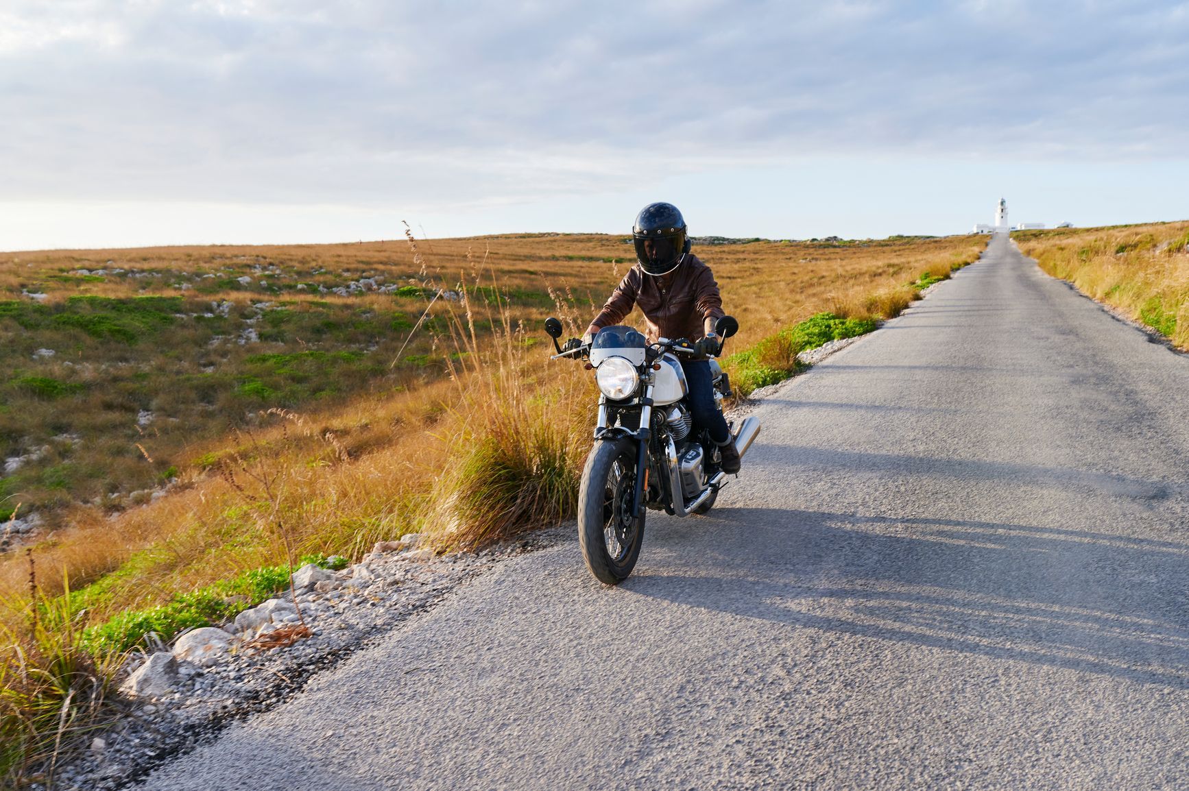 Motorista sa kacigom vozi motor na putu kroz osunčanu ravnicu.