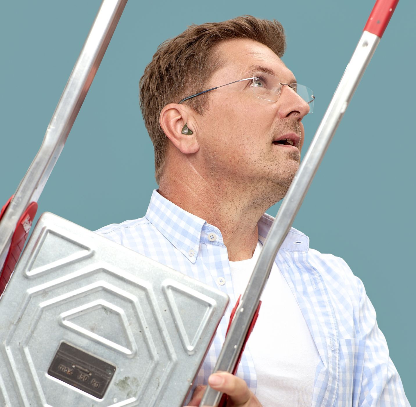 Muskarac sa zastitom sluha za slobodno vreme i rad drzi merdevine