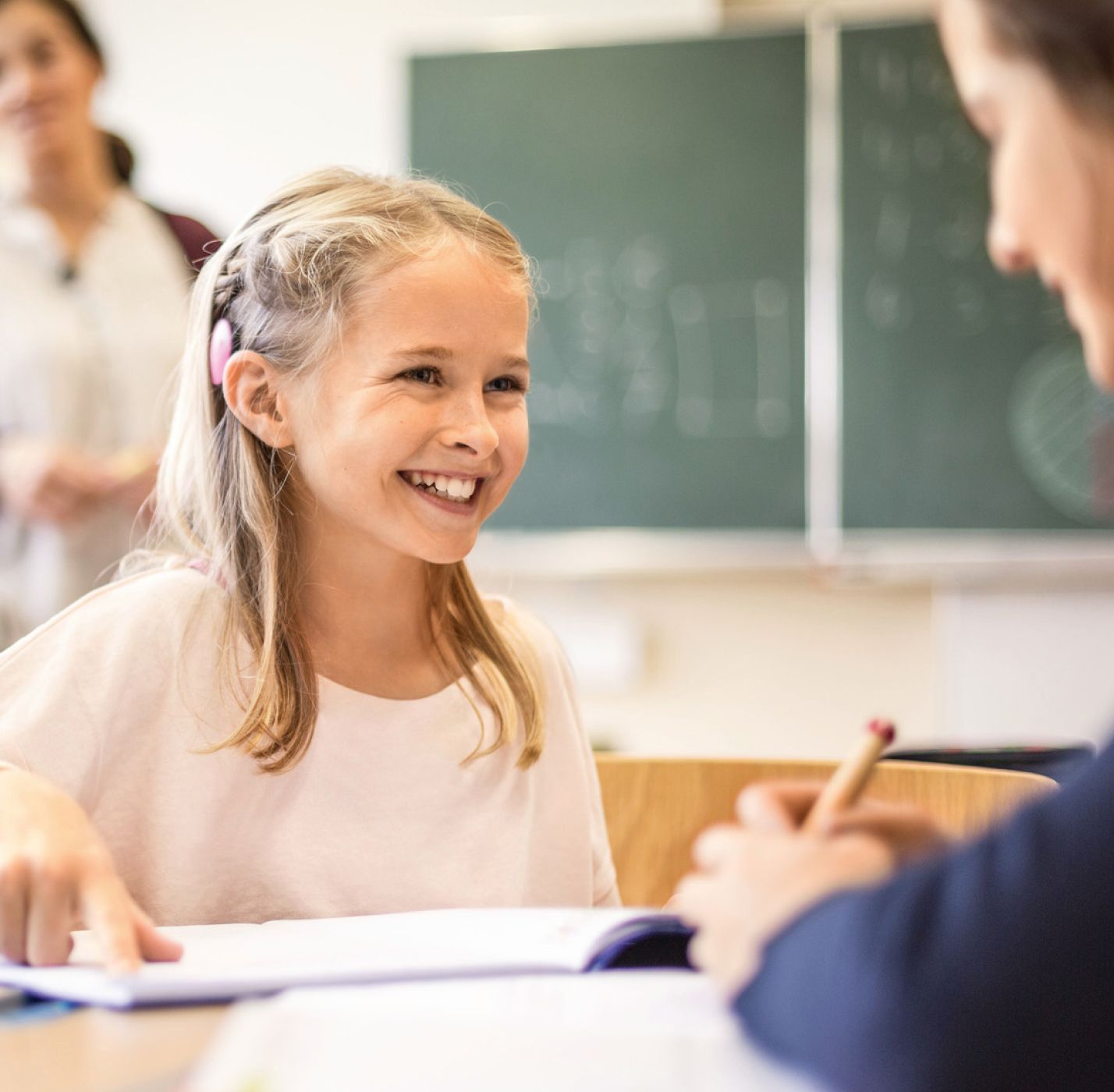 Nasmejana plavokosa devojcica u skolskoj klupi