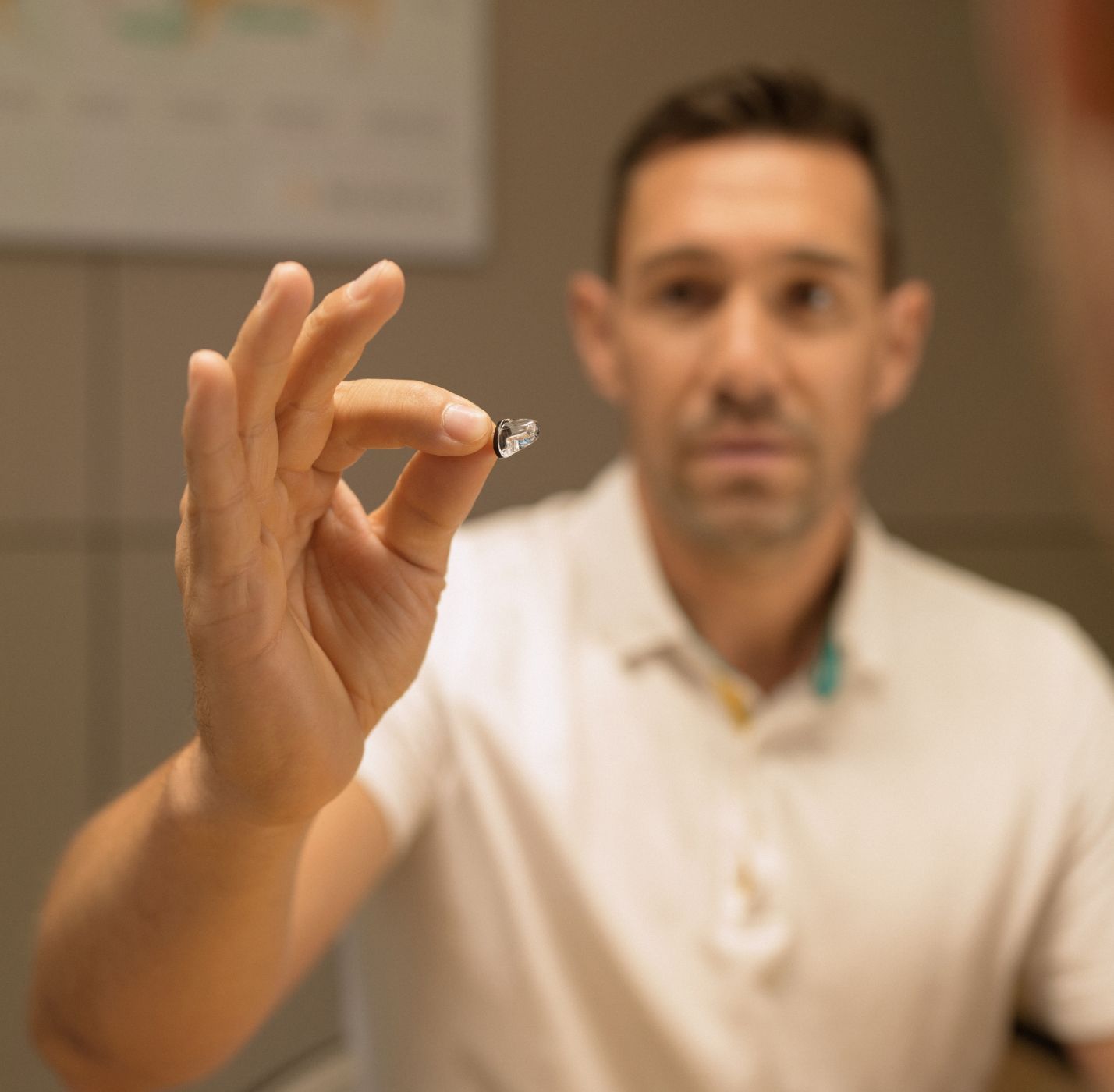 Neuroth akustičar drži slušni aparat u ruci i pozorno ga gleda s usredotočenim izrazom lica