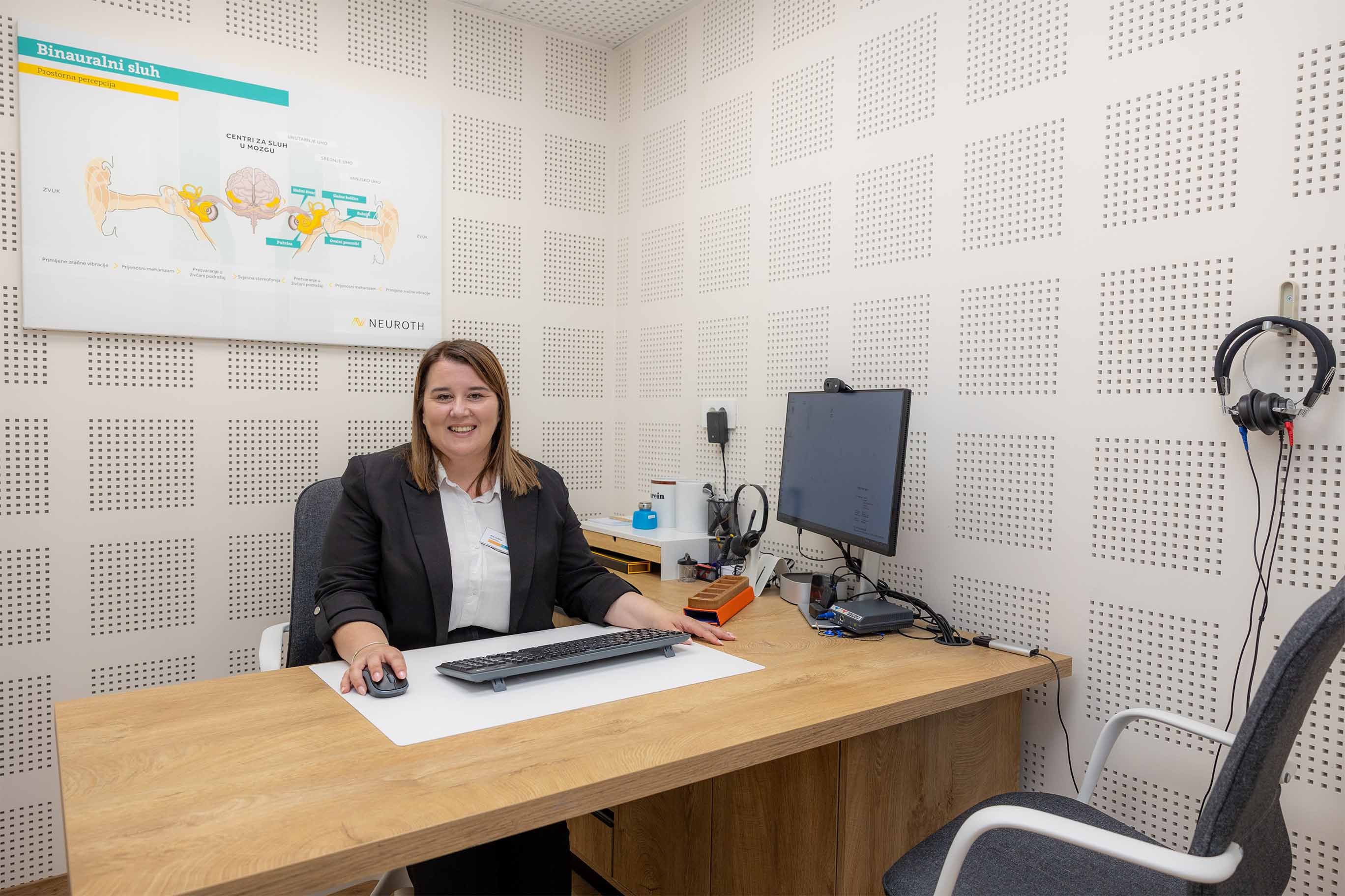 Nasmijana Neuroth akusticarka sjedi za stolom u slusnom centru