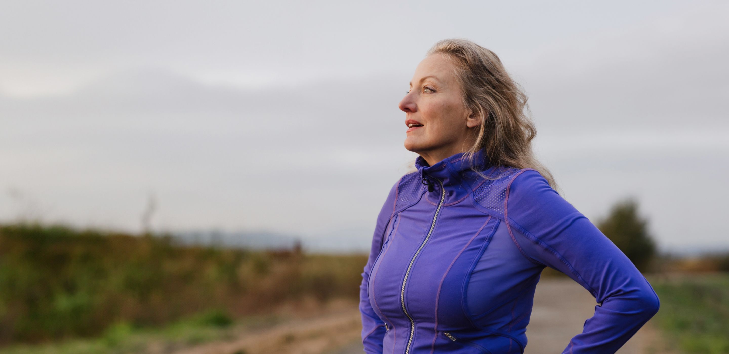 Starija zena plave kose u sportskoj jakni ljubicaste boje stoji napolju